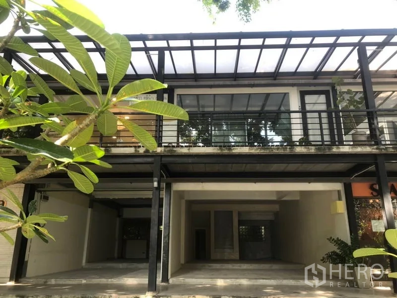 零售空间 出租在Watthana, Bangkok - 两层零售铺面，钢结构雨棚与整面玻璃门头，入口绿植环绕。