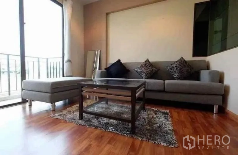 ทาวน์เฮาส์ ให้เช่า - ห้องพักผ่อนชั้นบน โซฟาสีเทา โต๊ะกลาง และทางออกสู่ระเบียงกระจกบานเลื่อน