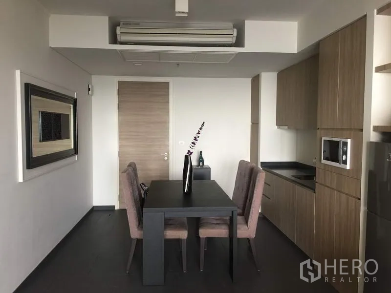 Condominium for rent or sale in Bang Lamung, Chon Buri - Modern dining area for four beside a compact kitchen with wood cabinets and built-in microwave.