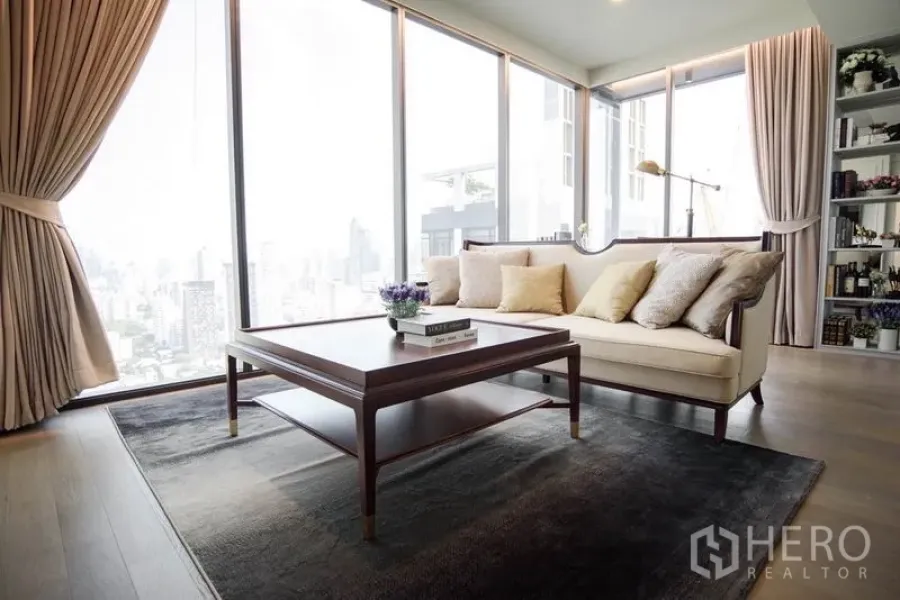 Condominium for rent or sale in Watthana, Bangkok - Bright living room with floor-to-ceiling windows, beige sofa, wood coffee table and city skyline view.