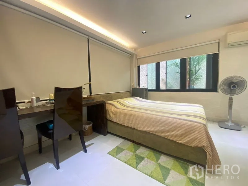 Detached House for sale in Khlong Toei, Bangkok - Cozy bedroom with large windows, roller blinds, and built-in work desk.