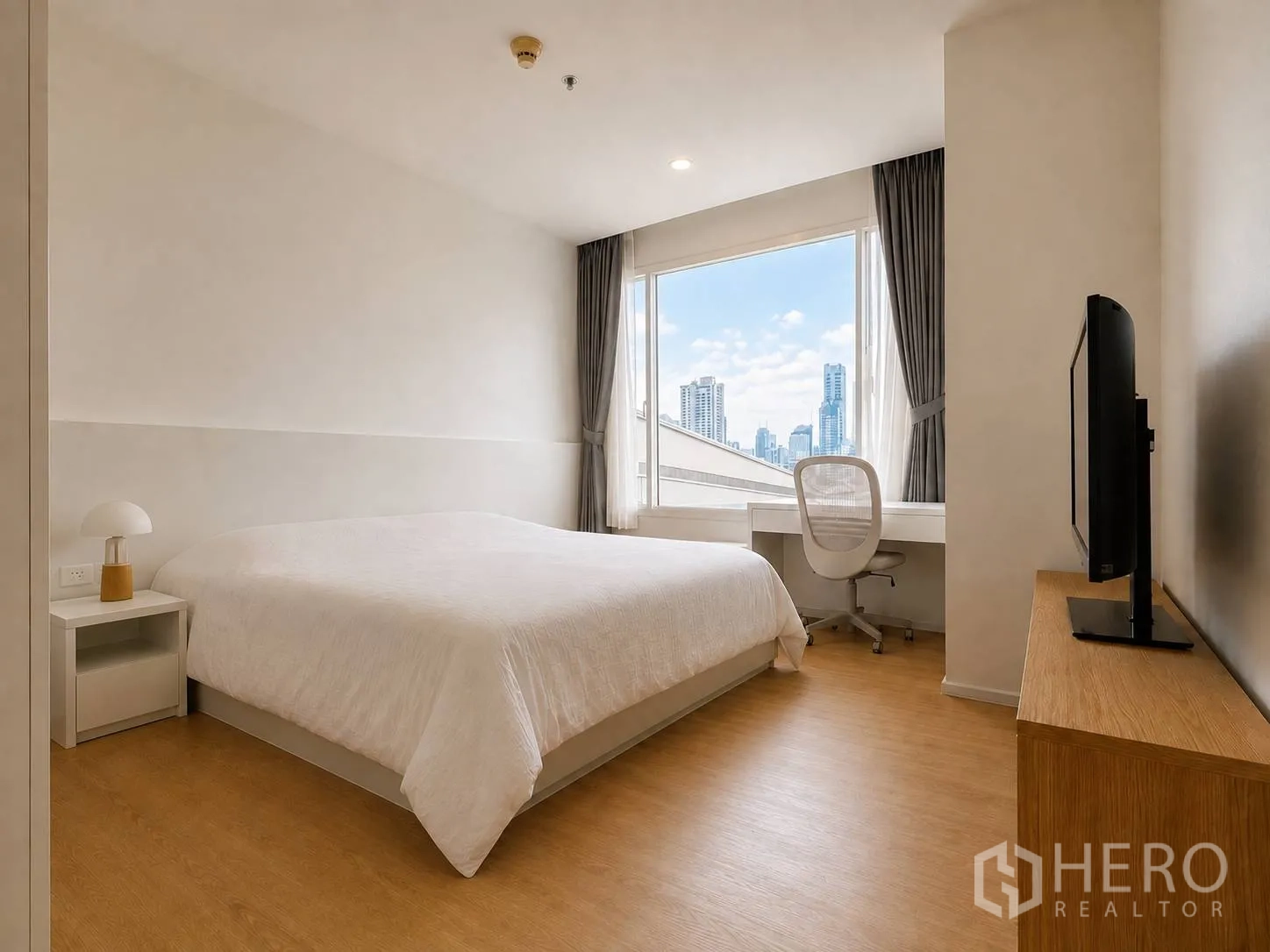 Condominium for rent or sale in Watthana, Bangkok - Bright bedroom with large bed, desk by a wide window showing city skyline views and a TV on a console.