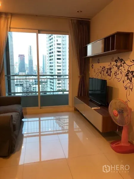 Condominium for sale in Ratchathewi, Bangkok - Living room facing the balcony with skyline view, TV console and glossy tile floors.