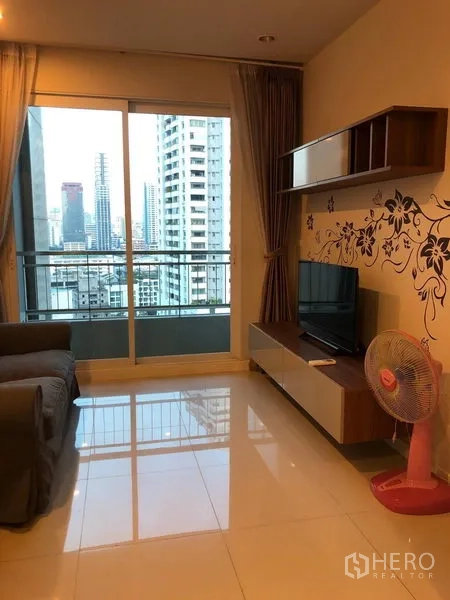 Condominium for sale in Ratchathewi, Bangkok - Living room facing the balcony with skyline view, TV console and glossy tile floors.