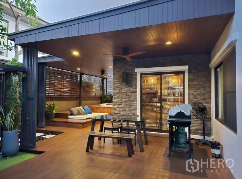 独立式住宅 出租在Bang Phli, Samut Prakan - 傍晚的有顶露台，烧烤区与餐桌灯光温暖