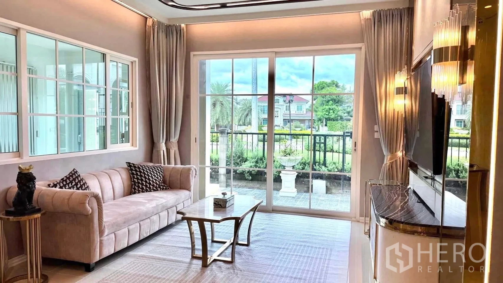 Detached House for rent or sale in Bueng Kum, Bangkok - Living area with pastel sofa and glass coffee table facing wide sliding doors to greenery.