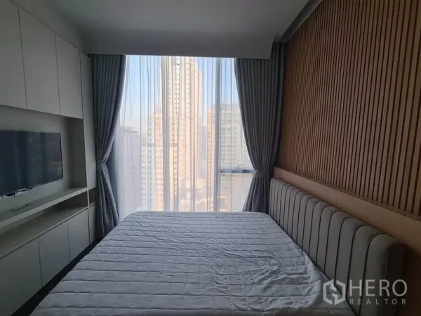 Condominium for rent in Watthana, Bangkok - Bedroom with floor-to-ceiling window, city skyline view, and built-in TV cabinet.