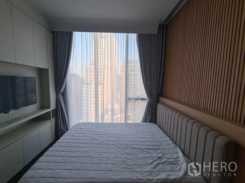 Condominium for rent in Watthana, Bangkok - Bedroom with floor-to-ceiling window, city skyline view, and built-in TV cabinet.
