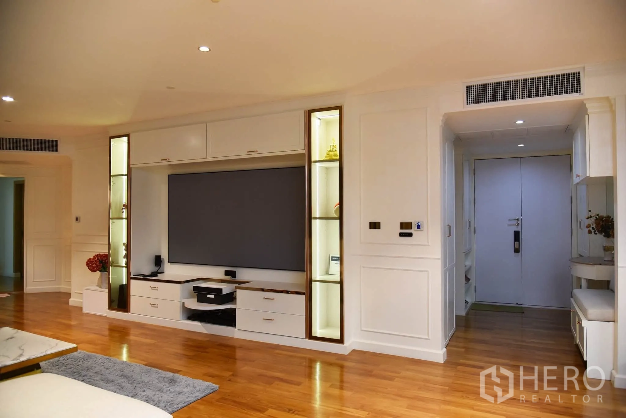 Condominium for sale in Khlong San, Bangkok - Living room with a built-in media wall, display shelves, and warm wooden floors near the entry.
