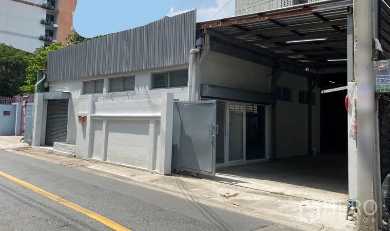 Warehouse for rent in Chatuchak, Bangkok - Corner view of the warehouse showing a roller shutter, sliding gate, and covered loading bay.