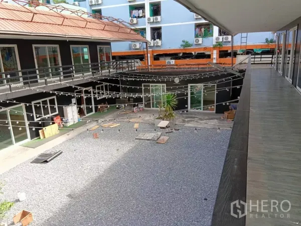 零售空间 出租在Huai Khwang, Bangkok - 双层零售楼围合碎石庭院，串灯与推拉玻璃门清晰可见。