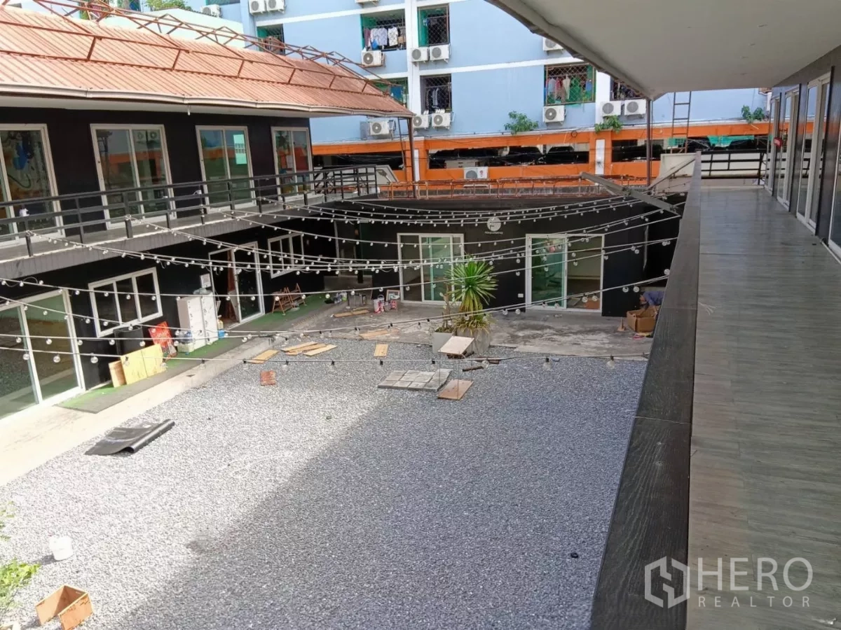 零售空间 出租在Huai Khwang, Bangkok - 双层零售楼围合碎石庭院，串灯与推拉玻璃门清晰可见。