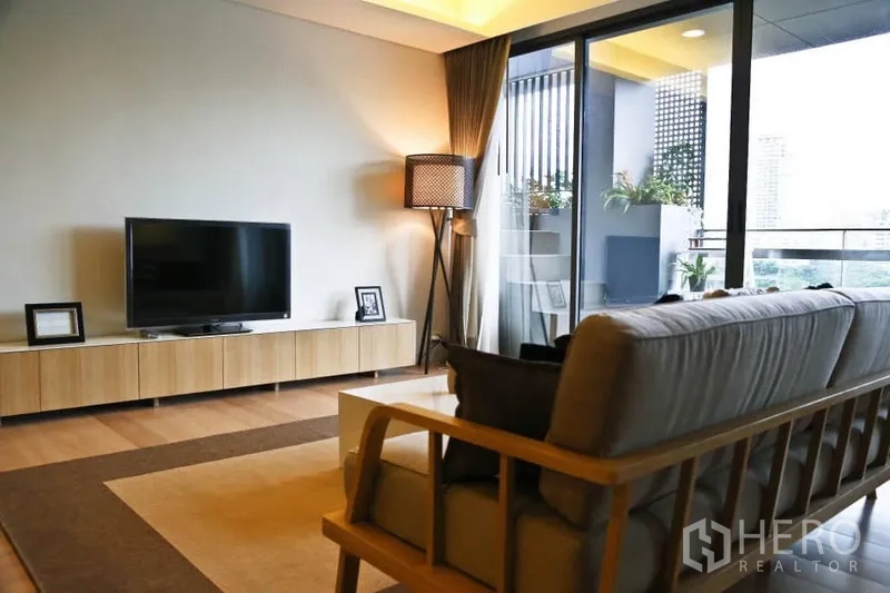 Condominium for rent in Watthana, Bangkok - Cozy living room with sofa, TV console and floor lamp opening to a balcony.