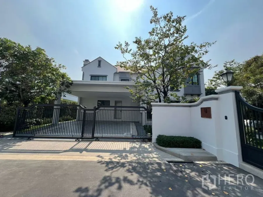 Detached House for rent in Saphan Sung, Bangkok - Front view of a modern two-storey white house with gated driveway and trees.