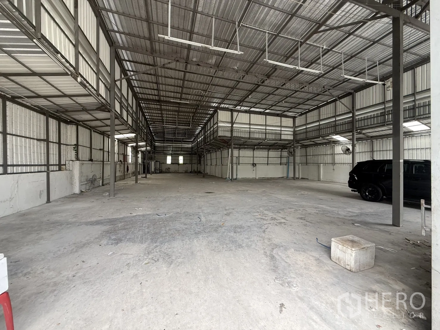 Warehouse for rent in Huai Khwang, Bangkok - Open warehouse interior with high roof, concrete floor, side mezzanine platforms and wall-mounted fans.