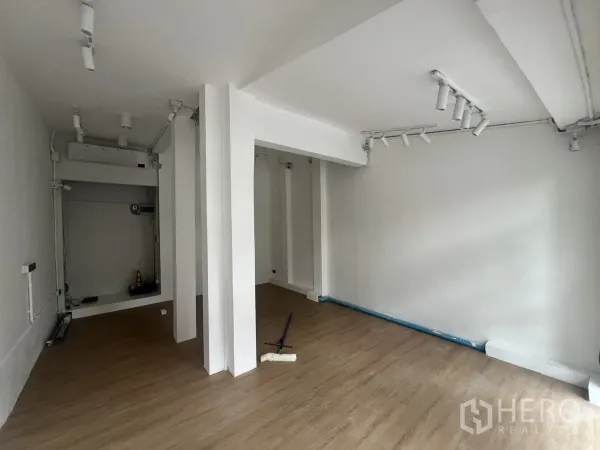 零售空间 出租在Watthana, Bangkok - 开放式零售室内，白色墙面、木纹地板、承重柱和轨道射灯。