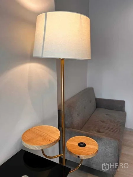 คอนโด ให้เช่าหรือขายในPathum Wan, Bangkok - โคมไฟตั้งพื้นพร้อมชั้นวางไม้คู่ถัดจากโซฟาสีเทา