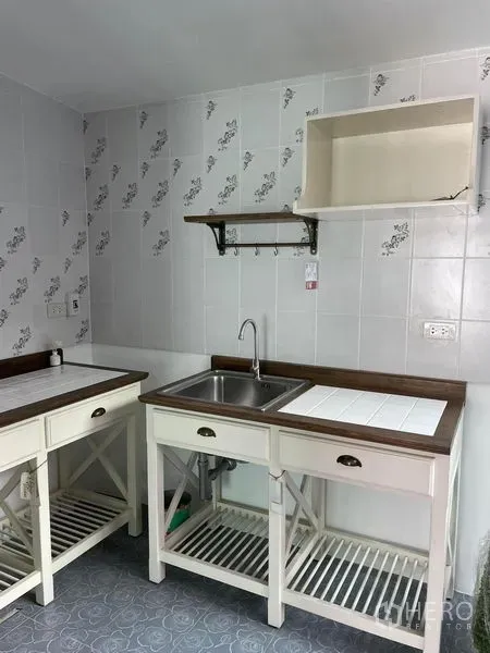 Townhouse for rent in Samut Prakan - Compact kitchen with white tiled walls, wooden countertops, stainless sink and open shelf storage.