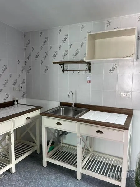 Townhouse for rent in Samut Prakan - Compact kitchen with white tiled walls, wooden countertops, stainless sink and open shelf storage.