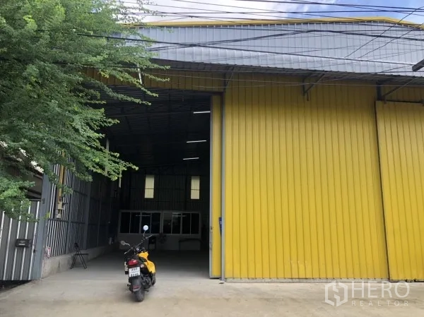 Warehouse for rent in Wang Thonglang, Bangkok - Warehouse exterior with tall entry door and covered access, with small parking area in front.