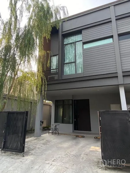 Townhouse for rent in Saphan Sung, Bangkok - Modern two-storey townhouse exterior with grey facade, tall windows and a gated driveway with covered carport.