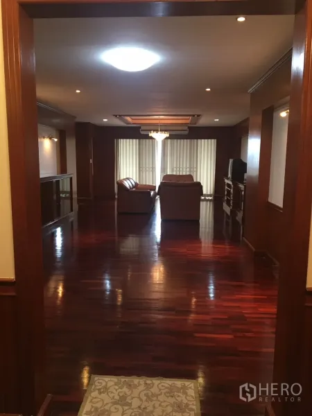 คอนโด ให้เช่าในWatthana, Bangkok - มุมมองทางเข้าไปยังห้องนั่งเล่นกว้าง พื้นไม้เงางาม โซฟาหนัง โคมระย้า และม่านบานเลื่อน ในคอนโดเขตวัฒนา กรุงเทพฯ