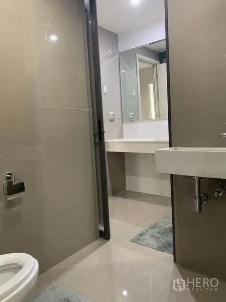 คอนโด ให้เช่าในKhlong Toei, Bangkok - ห้องน้ำโทนเบจพร้อมอ่างล้างหน้าติดผนัง กระจกบานใหญ่ และโถสุขภัณฑ์