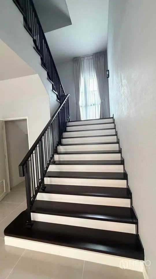 Detached House for rent in Bang Phli, Samut Prakan - Staircase with black handrail and white risers beside a tall window.