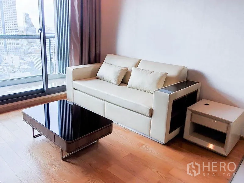 公寓 出租在Bang Rak, Bangkok - 客厅配米色沙发与茶几，推门连通阳台，可观城市景观。