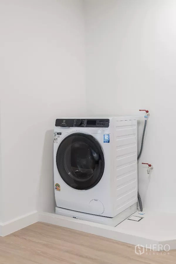 Apartment for rent - Compact laundry nook with a front-loading washing machine on a raised platform.