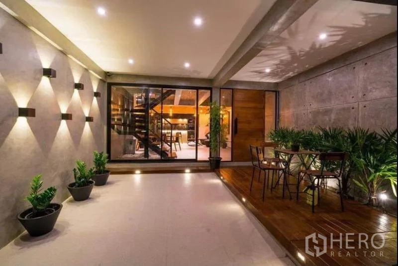 ทาวน์เฮาส์ ให้เช่าในKhlong Toei, Bangkok - ชานระเบียงมีหลังคาพร้อมไฟติดผนัง กระถางต้นไม้ และประตูบานเลื่อนเข้าสู่โถงรับแขก