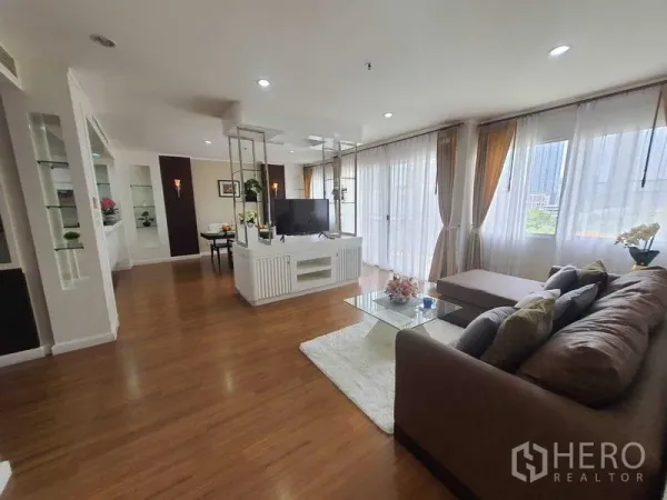 房间 出租在Watthana, Bangkok - 采光充足的客厅，L形沙发、玻璃茶几与纱帘落地窗