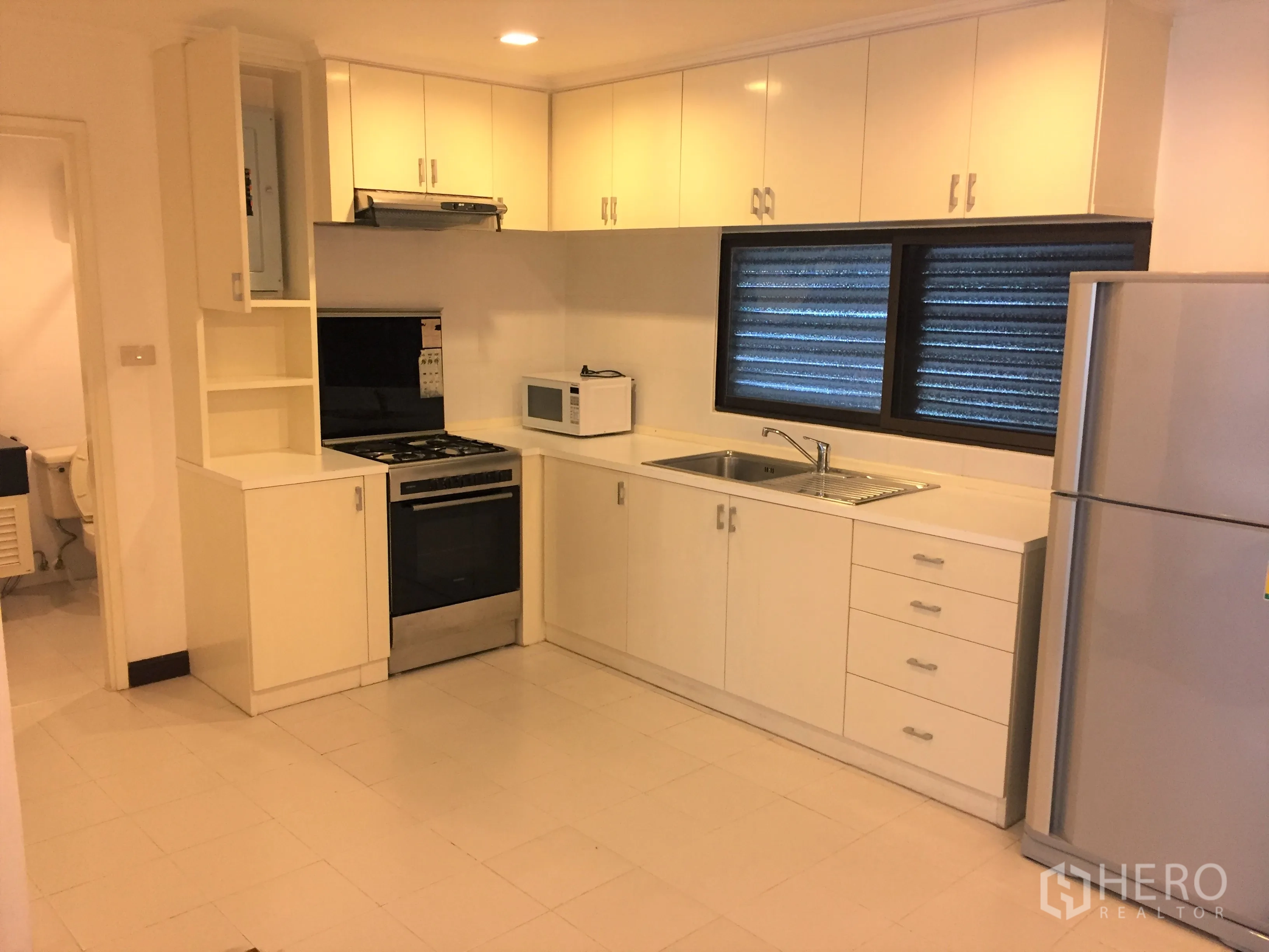 Condominium for rent in Watthana, Bangkok - White fitted kitchen with gas stove, oven, microwave, double sink and full-size refrigerator.