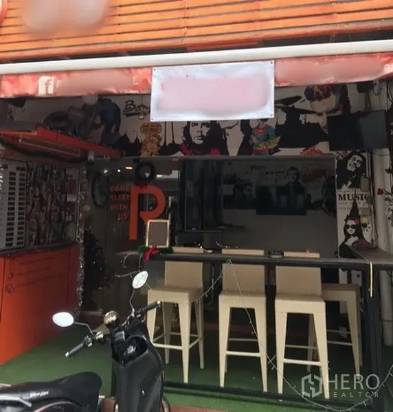零售空间 出租在Watthana, Bangkok - 临街小型商铺外观，橙色雨棚、整面玻璃、吧台与高脚椅，流行艺术风格墙面，靠近Phrom Phong站。