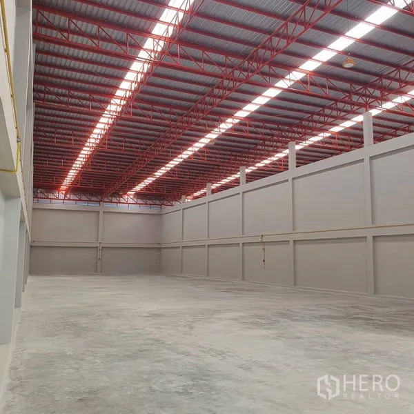 Warehouse for rent in Mueang Samut Sakhon, Samut Sakhon - Spacious warehouse interior with 10–12 m high ceiling, red steel trusses and skylight panels in Mueang Samut Sakhon.