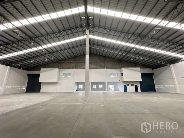 工厂 出租在Khlong Luang, Pathum Thani - 仓库内景，面向办公室区与大型蓝色卷帘装卸门。