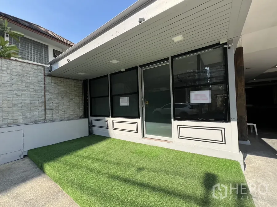 零售空间 出租在Watthana, Bangkok - 街边玻璃店面，黑色窗框与推拉门，门前有人造草坪与雨棚