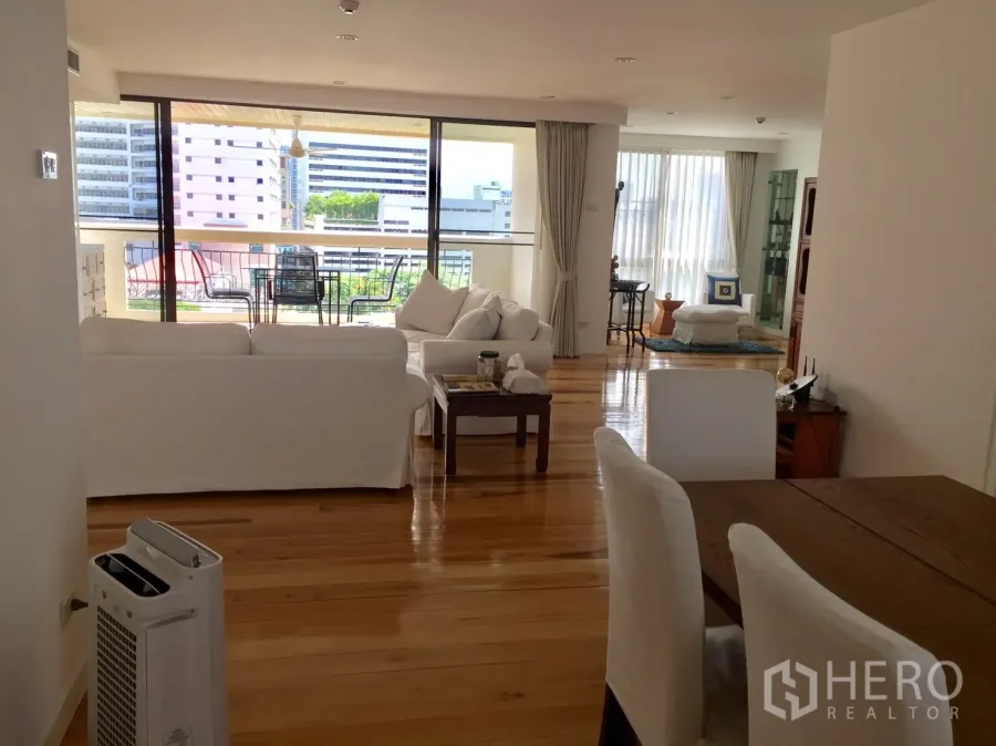 Condominium for rent in Watthana, Bangkok - Bright open-plan living room with white sofas, polished wood floors and a large balcony with outdoor dining and city views.