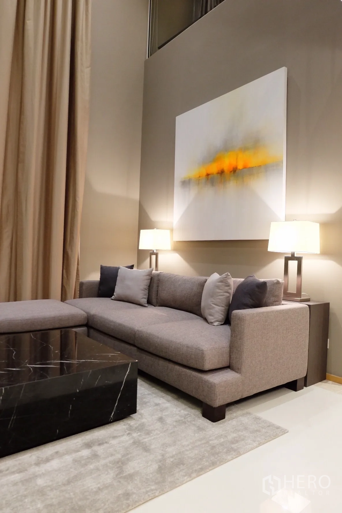 Condominium for rent in Sathon, Bangkok - Cozy sectional sofa beneath abstract artwork with double-height wall and warm table lamps.
