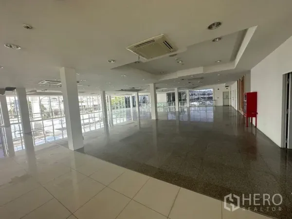 Retail Space for rent in Prawet, Bangkok - Large retail floor with mixed tile finishes, a red fire safety cabinet, and wraparound windows.
