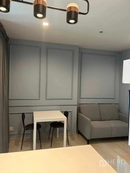 คอนโด ขายในPathum Wan, Bangkok - มุมนั่งเล่นมีโซฟาสีเทาและโต๊ะทานอาหารสองที่นั่ง ตกแต่งผนังบัวคลาสสิก