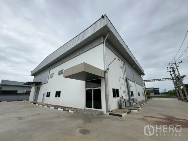 Factory for sale in Bang Bo, Samut Prakan - Corner view of factory building with glass entry, side driveway and AC units.