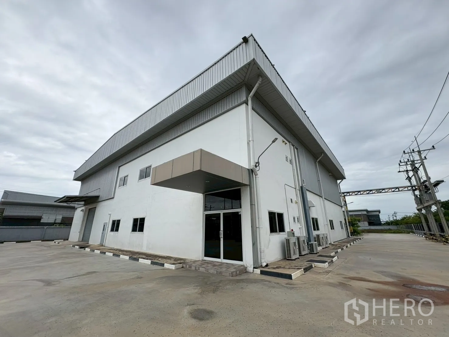 Factory for sale in Bang Bo, Samut Prakan - Corner view of factory building with glass entry, side driveway and AC units.