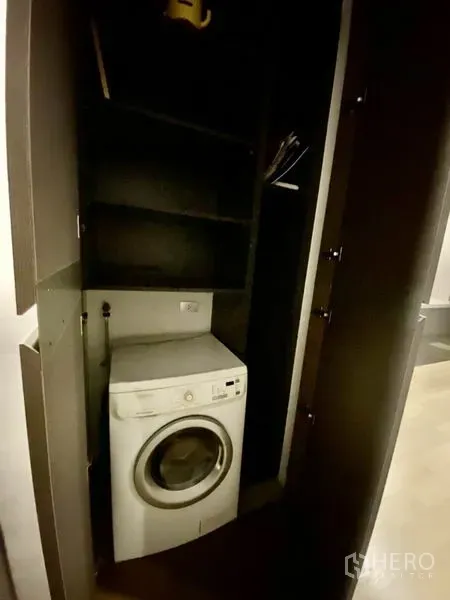 Condominium for rent or sale in Bang Rak, Bangkok - Built-in laundry cabinet with front-loading washing machine and shelving.