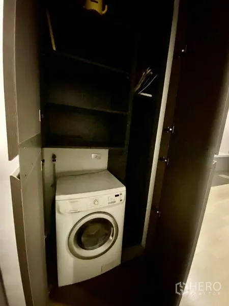 Condominium for rent or sale in Bang Rak, Bangkok - Built-in laundry cabinet with front-loading washing machine and shelving.