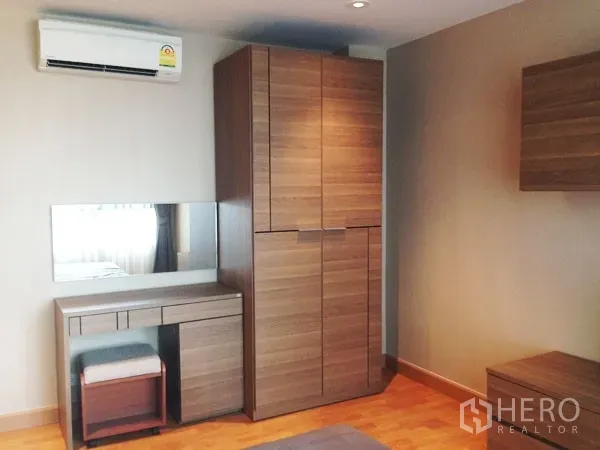 Condominium for rent or sale in Mueang Samut Prakan, Samut Prakan - Bedroom corner with tall wardrobe, dressing table, mirror and wall air-conditioner.