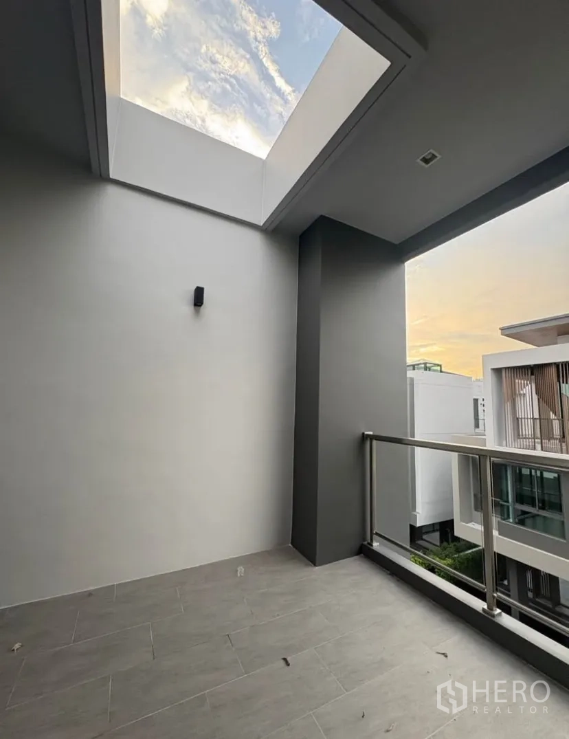 Detached House for rent in Suan Luang, Bangkok - Covered balcony with skylight and metal railing overlooking neighboring modern homes at sunset.