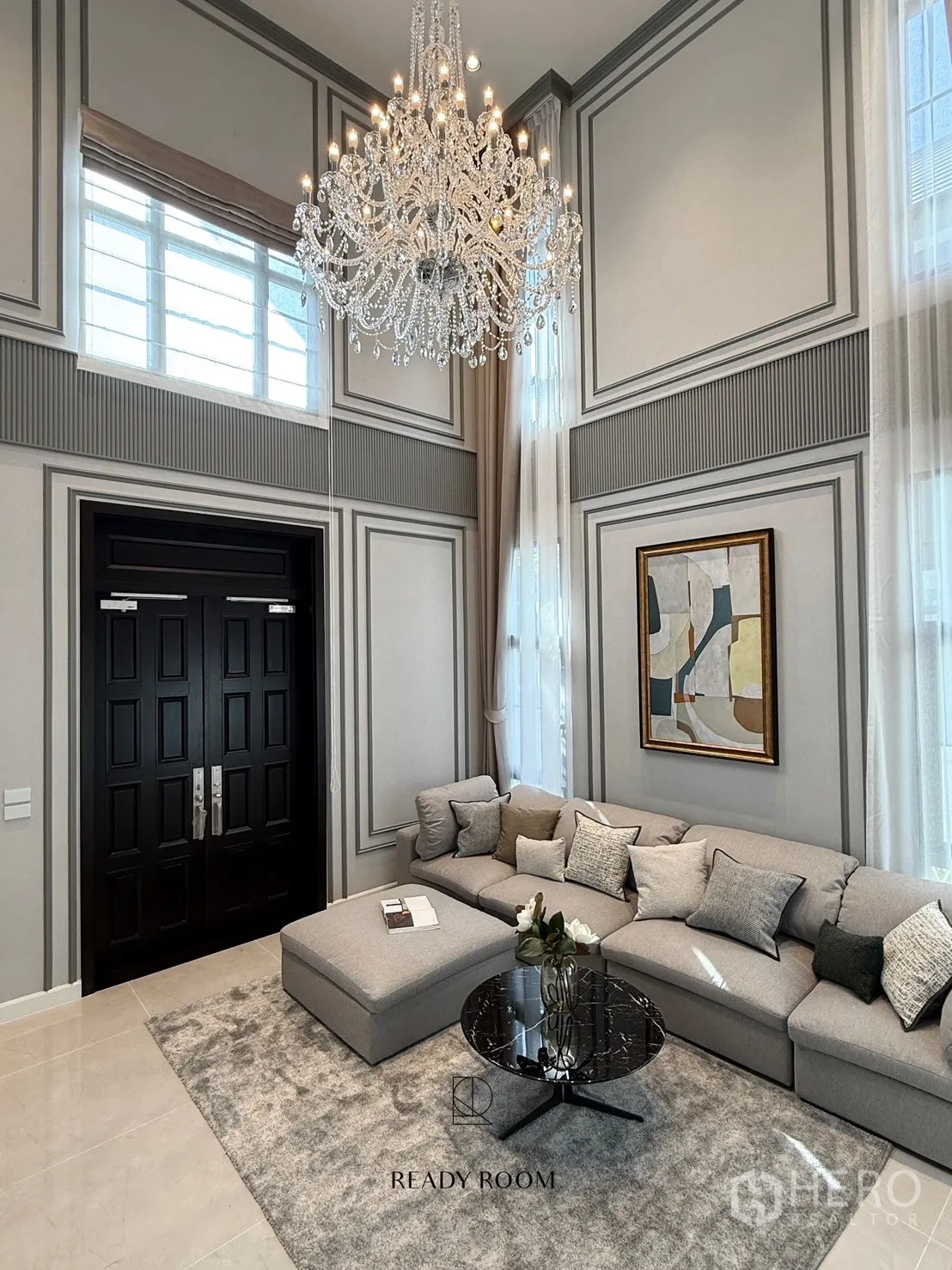 บ้าน ให้เช่าหรือขายในBang Phli, Samut Prakan - ห้องนั่งเล่นเพดานสูงสองชั้น โคมระย้าขนาดใหญ่ หน้าต่างสูง และโซฟาเข้ามุมสีเทา