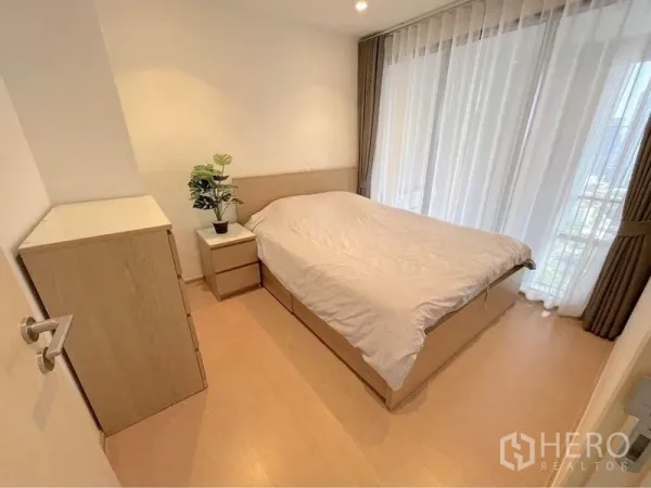 Condominium for rent in Watthana, Bangkok - Bright bedroom with double bed, bedside table, dresser, and floor-to-ceiling curtains.