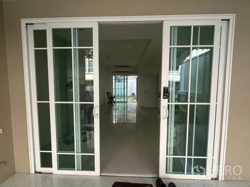 带办公室的家 出租在Bang Na, Bangkok - 白框推拉玻璃门入口，通向长条形瓷砖走廊。